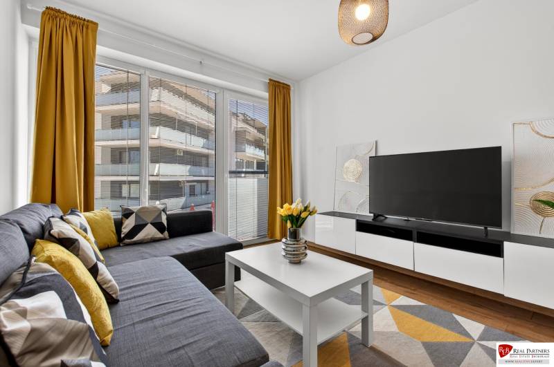 Predaj 2-izbový byt GREEN VILLAGE, 51m2, loggia, Dunajská Lužná - Dvojizbový byt s veľkými oknami, pohovkou, televízorom, žltými závesmi a podlahou s dreveným dekorom.