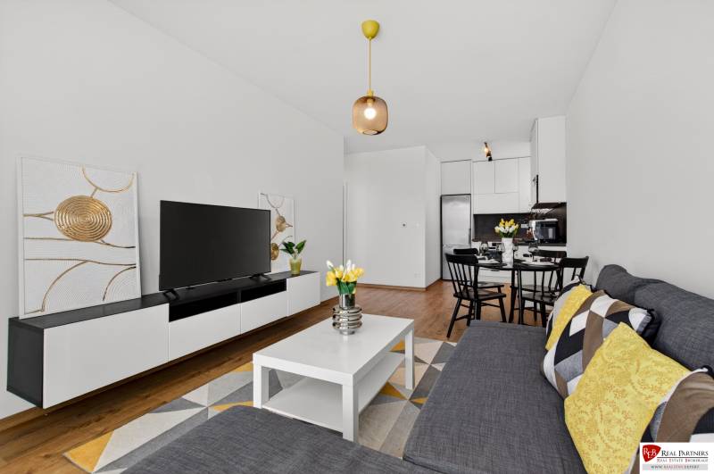Predaj 2-izbový byt GREEN VILLAGE, 51m2, loggia, Dunajská Lužná - Obývacia izba v 2-izbovom byte s podlahou s dreveným dekorom, pohovkou a televízorom.