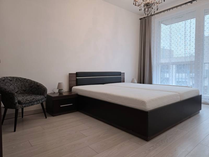 PRENÁJOM - 3 izbový byt v novostavbe - Nitra, blízko centra - Spálňa v 3-izbovom byte s posteľou, kreslom a podlahou s dreveným dekorom.