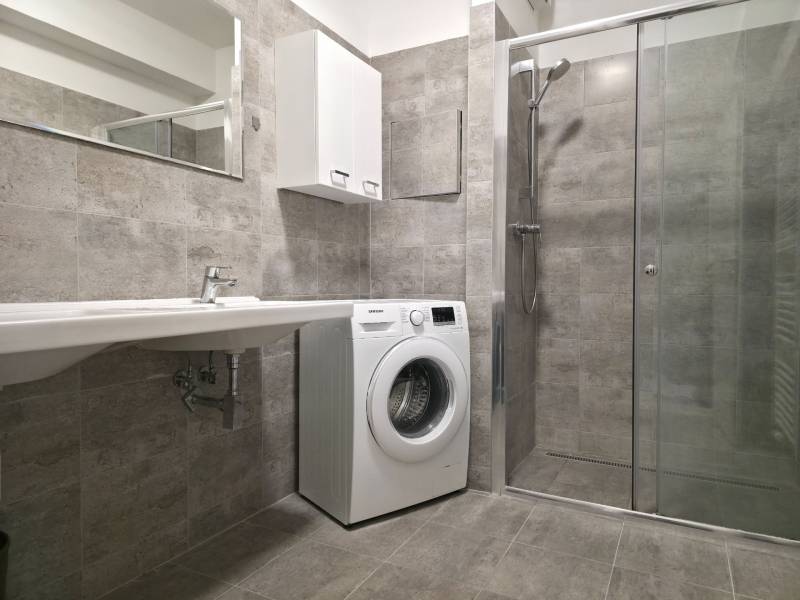 PRENÁJOM - 3 izbový byt v novostavbe - Nitra, blízko centra - Kúpeľňa v 3-izbovom byte s práčkou, sprchovým kútom a umývadlom na šedých obkladoch.