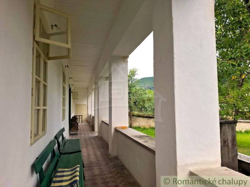 Unikátny meštiansky dom s veľkou záhradou – história, štýl a potenciál - Veranda s lavicou pri rodinnom dome v Dobroči, výhľad na záhradu a stromy.
