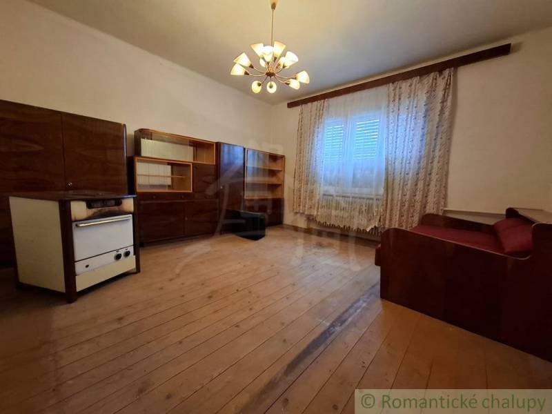 Pôvodný päťizbový rodinný dom s hospodárskymi budovami blízko centra o - Obývacia izba v rodinnom dome s dreveným dekorom, záclonami a pohovkou.