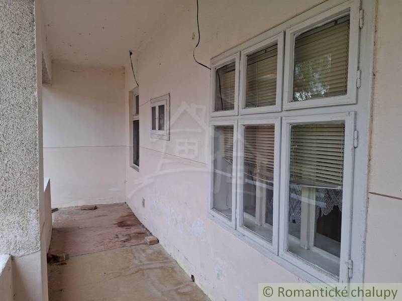 Pôvodný päťizbový rodinný dom s hospodárskymi budovami blízko centra o - Rodinný dom v Mužli s priechodnou terasou, oknami so žalúziami a betónovou podlahou.