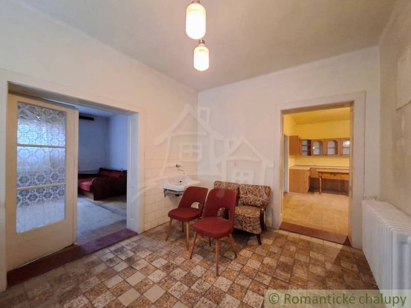 Pôvodný päťizbový rodinný dom s hospodárskymi budovami blízko centra o - Interiér rodinného domu s kreslami, umývadlom, kuchyňou a dvomi otvorenými dverami.