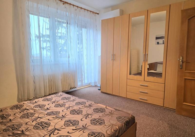 PRENÁJOM - Priestranný 3 izbový byt - Nitra, Centrum - Spálňa s veľkým oknom, záclonami a drevenou skriňou v 3-izbovom byte.