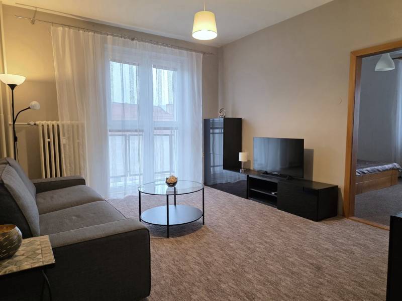 PRENÁJOM - Priestranný 3 izbový byt - Nitra, Centrum - Obývačka v 3-izbovom byte s pohovkou, televízorom, stolíkom a balkónovými dverami.