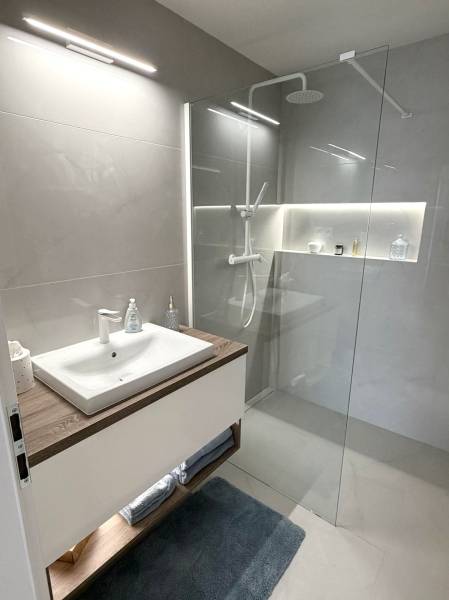 2 izbový A.3.1.- 58,91 m2 Bell Residence  - Kúpeľňa s umývadlom, skleneným sprchovým kútom a svetlými dlaždicami v 2-izbovom byte.