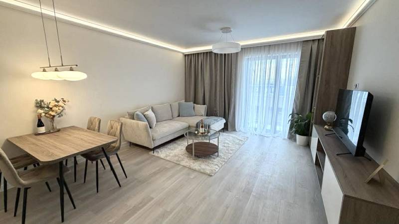 2 izbový A.3.1.- 58,91 m2 Bell Residence  - Obývacia izba v 2-izbovom byte s podlahou s dreveným dekorom, pohovkou a jedálenským stolom.