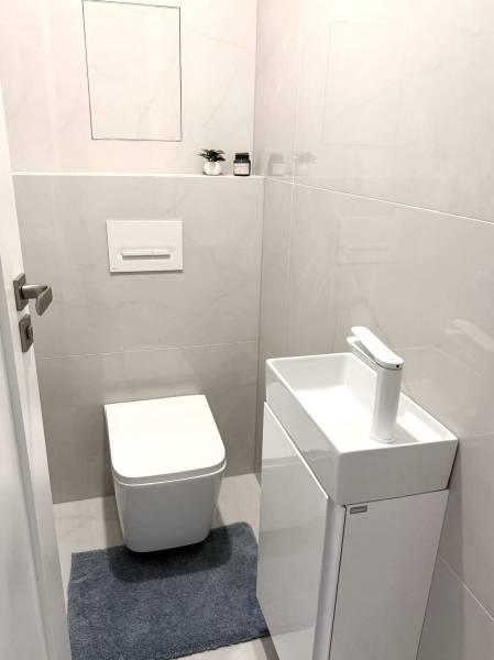 2 izbový A.3.1.- 58,91 m2 Bell Residence  - Toaleta s umývadlom v 2-izbovom byte, svetlé obklady a modrý koberec.