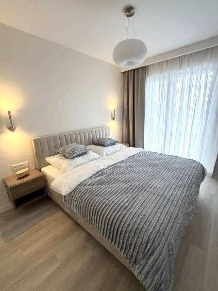 2 izbový A.3.1.- 58,91 m2 Bell Residence  - Spálňa v 2-izbovom byte s podlahou s dreveným dekorom, posteľou a závesmi.