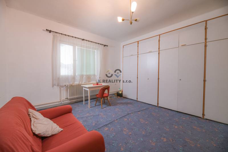 Na predaj rodinný dom Trnava, Zelenečská ulica, pozemok 1085 m2 - Rodinný dom obsahuje obývačku s kobercovou podlahou, oranžový gauč a biely stôl.