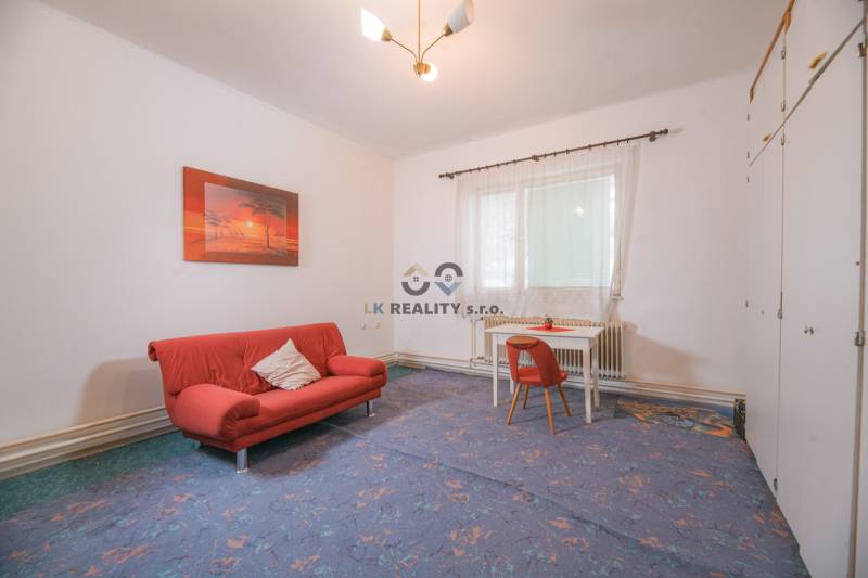 Na predaj rodinný dom Trnava, Zelenečská ulica, pozemok 1085 m2 - Obývacia izba v rodinnom dome s červenou pohovkou a stolom so stoličkou.