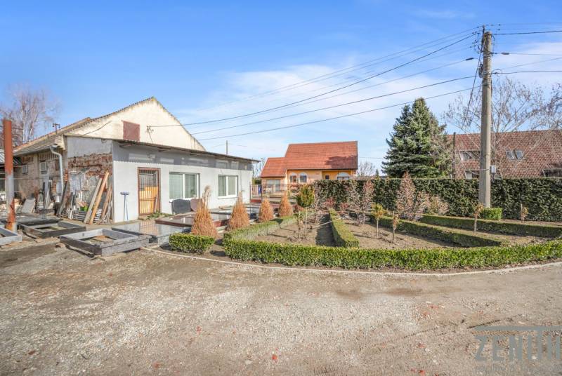 Komerčný objekt s pozemkom – možnosť zmeny na rodinný dom - Obchodné priestory v Okoči s úpravou záhrady, obklopené stromami a kríkmi.