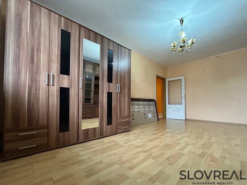 Na predaj 2i byt Levice - Svetlá obývacia izba s podlahou s dreveným dekorom a veľkou šatníkovou skriňou.