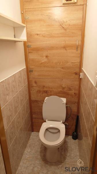 Na predaj 2i byt Levice - Toaleta so stenami obloženými dlažbou a dverami s dreveným dekorom v 2-izbovom byte.