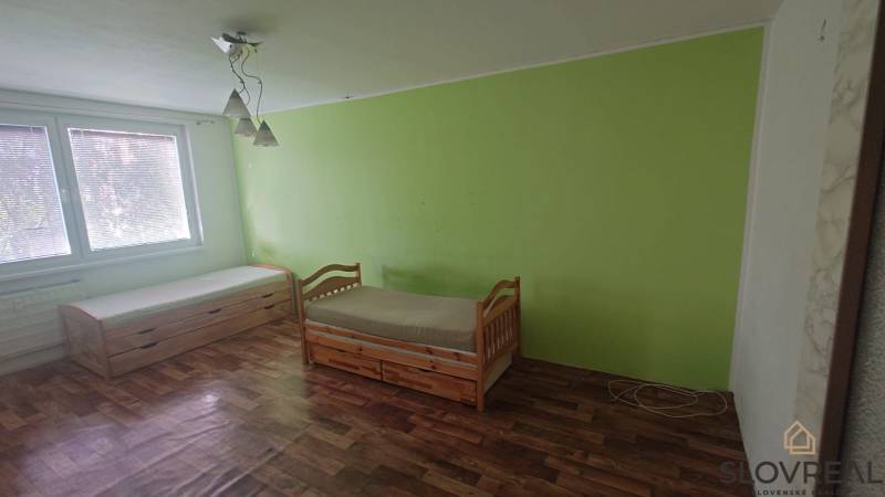 Na predaj 2i byt Levice - Interiér 2-izbového bytu s dvomi posteľami, podlaha s dreveným dekorom, zelená stena.