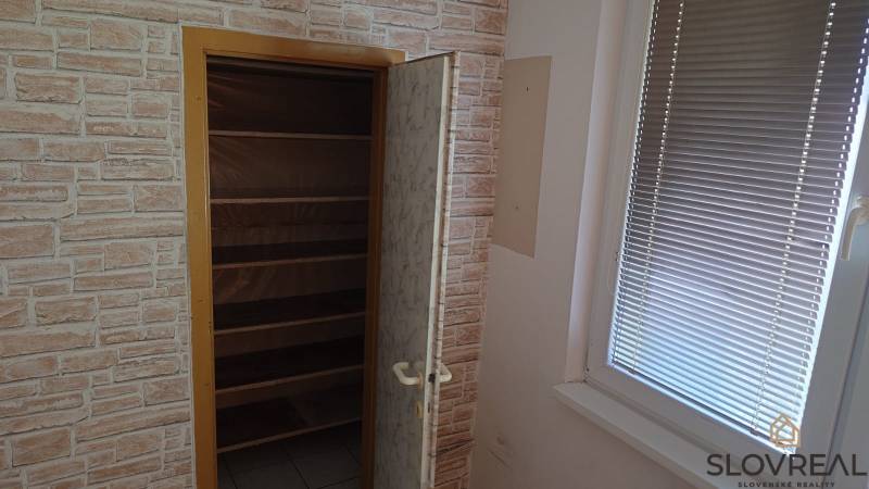 Na predaj 2i byt Levice - Skrinka s policami vedľa okna v 2-izbovom byte, priestor s imitáciou tehlovej steny.