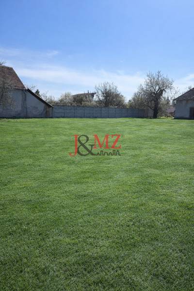 Na predaj výnimočný átriový rodinný dom s dvojgarážou v obci Dolná Seč - Záhrada v Dolnej Seči obklopená rodinnými domami a oplotením pod modrou oblohou.