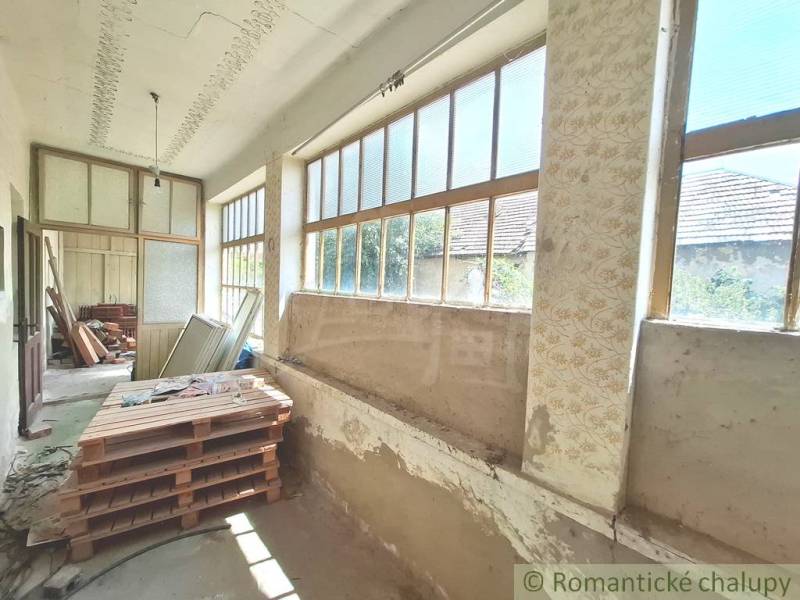 Rozľahlý pozemok so starým domom v obci Kamenný Most blízko Štúrova - Chata s priestrannou verandou, veľkými oknami a rozmanitým uskladneným materiálom.