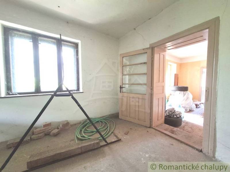 Rozľahlý pozemok so starým domom v obci Kamenný Most blízko Štúrova - Izba v chate so svetlom z okna, otvorenými dverami a stavebným neporiadkom.