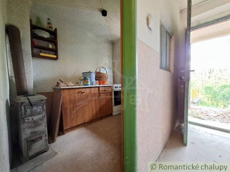 Pôvodná chata s panorámou nad korunami stromov blízko Hrona v rekreačn - Interiér chaty so starou pecou a nábytkom na podlahe s dreveným dekorom.