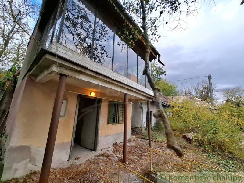 Pôvodná chata s panorámou nad korunami stromov blízko Hrona v rekreačn - Chata v Kameníne s preskleným balkónom, okolitá príroda a zarastený dvor.