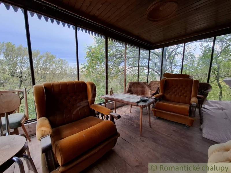 Pôvodná chata s panorámou nad korunami stromov blízko Hrona v rekreačn - Veranda s kreslami a podlahou s dreveným dekorom, chata obklopená zeleňou.