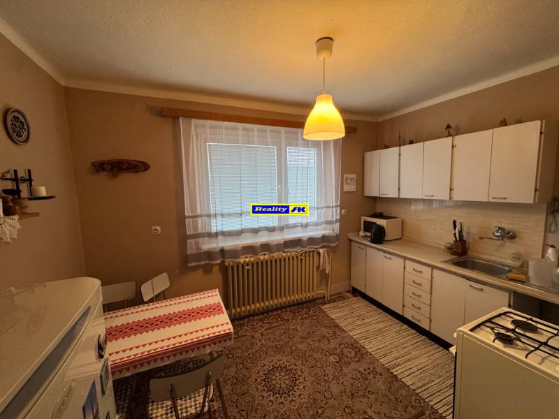 Rodinný dom Martin - Valča - Kuchyňa v rodinnom dome s bielymi skrinkami, vzorovaným kobercom a jedálenským stolom.