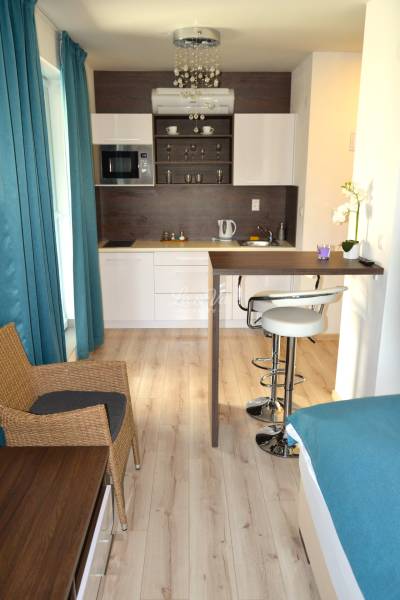 Na predaj apartmán s veľkou terasou Podhájská. - Garsónka s podlahou s dreveným dekorom, kuchynskou linkou a barovým pultom.