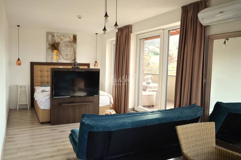 Na predaj veľký 49m2 apartmán Podhájská.  - Interiér 2-izbového bytu s podlahou s dreveným dekorom, televízorom a balkónom.