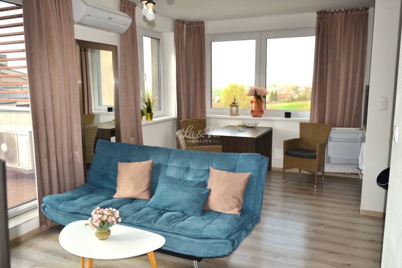 Na predaj veľký 49m2 apartmán Podhájská.  - Obývacia izba so sedačkou, stolíkom, rastlinami a podlahou s dreveným dekorom v 2-izbovom byte.