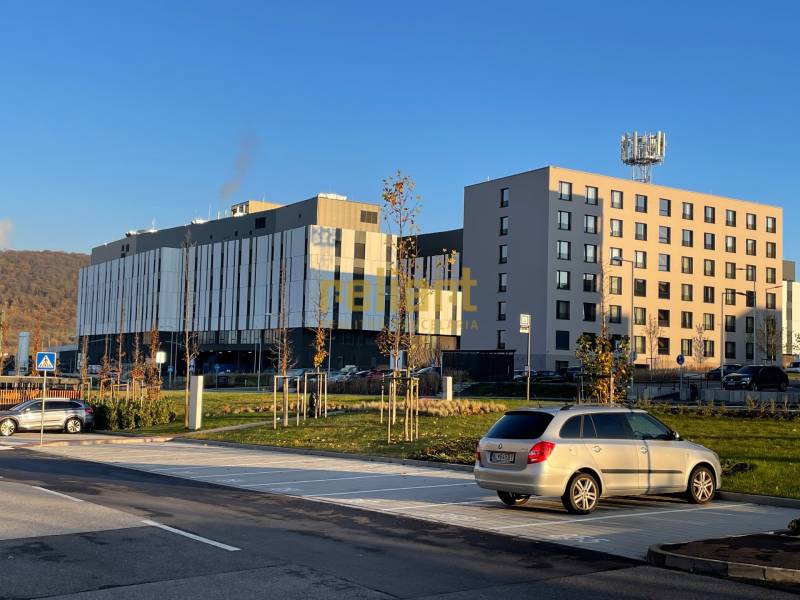 Bory:Na prenájom úplne nový, elegantný 2i byt/eng.text inside - Budovy na ulici Dominika v Lamači, Bratislava, obklopené parkoviskom a kopcami v pozadí.