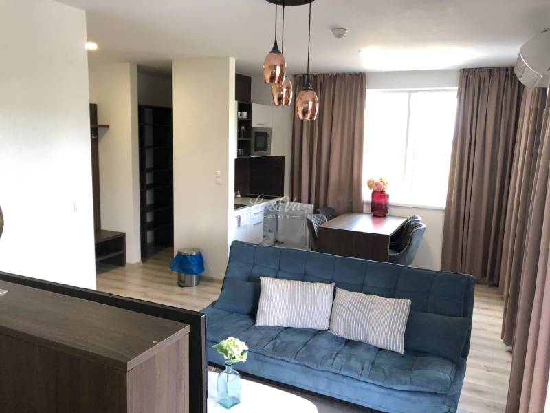 Na predaj štyri apartmány na jednom poschodí Podhájská - Obývacia izba v 2-izbovom byte s pohovkou a jedálenským stolom; podlaha s dreveným dekorom.