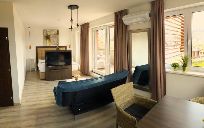 Na predaj štyri apartmány na jednom poschodí Podhájská - Svetlý 2-izbový byt s podlahou s dreveným dekorom, pohovkou a veľkými oknami.