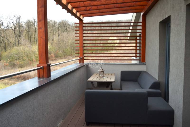 Na predaj štyri apartmány na jednom poschodí Podhájská - Balkón 2-izbového bytu s dreveným dekórom a výhľadom na zeleň.