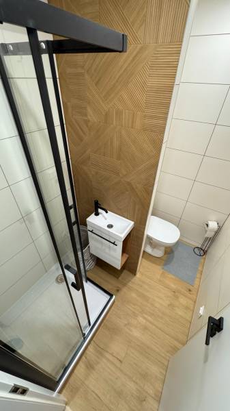 Exkluzívna ponuka moderného 1-izbového bytu s balkónom v meste Vráble - Kúpeľňa v 1-izbovom byte s podlahou s dreveným dekorom a sprchovacím kútom.