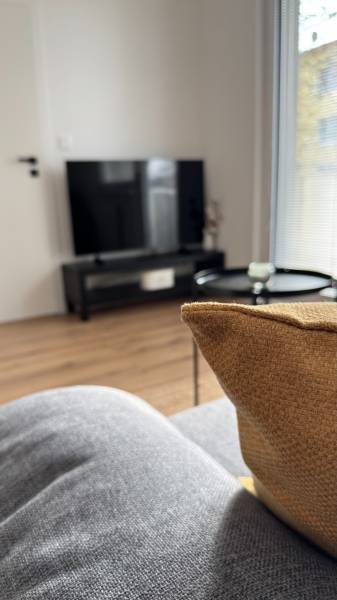 Exkluzívna ponuka moderného 1-izbového bytu s balkónom v meste Vráble - Obývacia izba v 1-izbovom byte s televíziou, sedačkou a podlahou s dreveným dekorom.