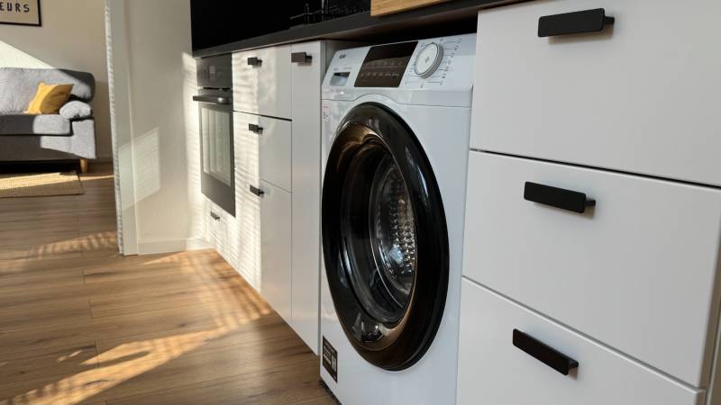 Exkluzívna ponuka moderného 1-izbového bytu s balkónom v meste Vráble - Kuchyňa v 1-izbovom byte so vstavanou práčkou a podlahou s dreveným dekorom.