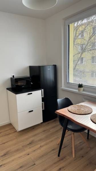 Exkluzívna ponuka moderného 1-izbového bytu s balkónom v meste Vráble - Kuchyňa v 1-izbovom byte s chladničkou, stolom a podlahou s dreveným dekorom.