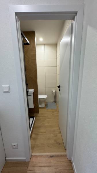 Exkluzívna ponuka moderného 1-izbového bytu s balkónom v meste Vráble - Kúpeľňa s toaletou a sprchovacím kútom v 1-izbovom byte, podlaha s dreveným dekorom.