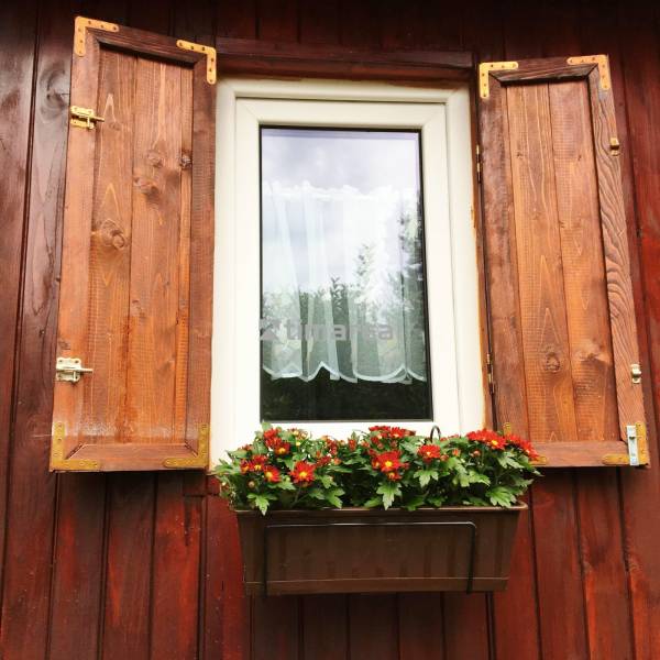 Bývanie v prírode, na dosah mesta, murov. chatka s celoročným využitím - Okno rodinného domu v Bohdanovciach nad Trnavou s okenicami a kvetináčom s červenými kvetmi.