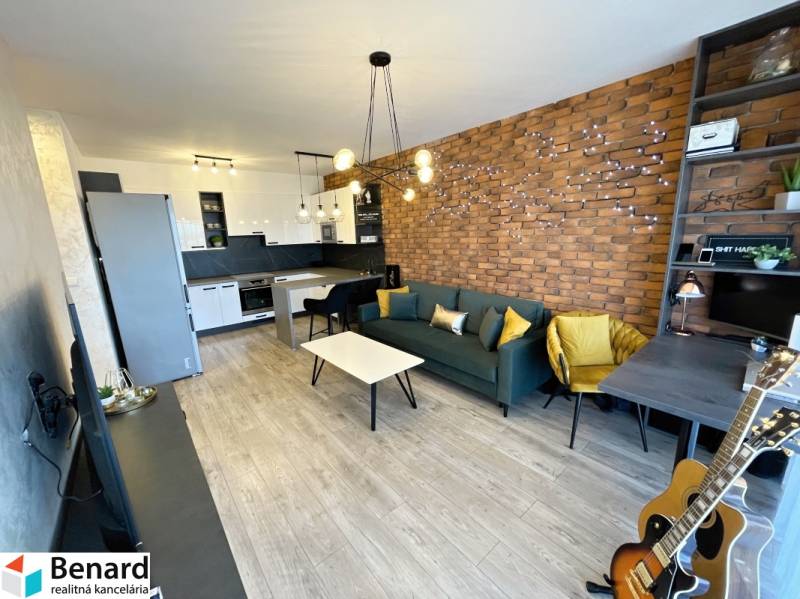 KOŠICE-2 IZBOVÝ BYT,NOVOSTAVBA,KOMPLET ZARIADENÝ,VL.PARK. MIESTO - Obývacia časť 2-izbového bytu s tehlovou stenou, podlahou s dreveným dekorom a kuchynským kútom.