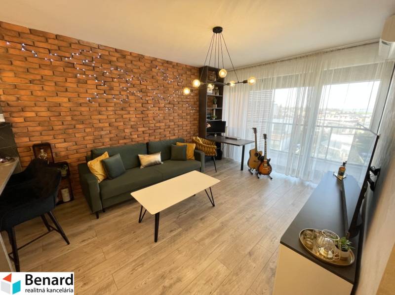 KOŠICE-2 IZBOVÝ BYT,NOVOSTAVBA,KOMPLET ZARIADENÝ,VL.PARK. MIESTO - Obývacia izba v 2-izbovom byte s tehlovým obkladom a podlahou s dreveným dekorom.