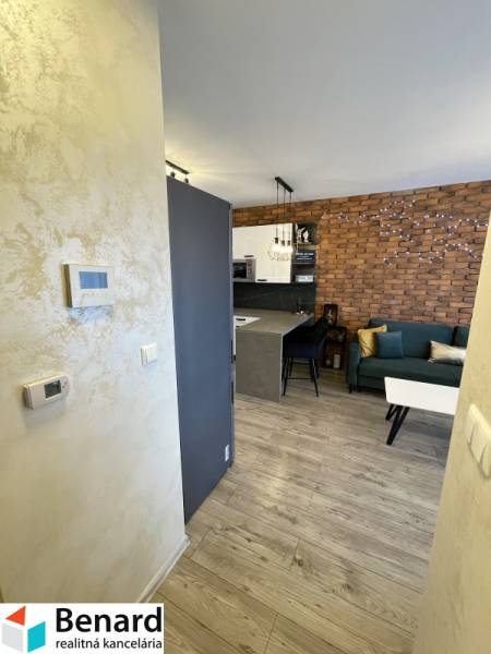 KOŠICE-2 IZBOVÝ BYT,NOVOSTAVBA,KOMPLET ZARIADENÝ,VL.PARK. MIESTO - Interiér 2-izbového bytu s podlahou s dreveným dekorom, tehlovou stenou a kuchynským kútom.