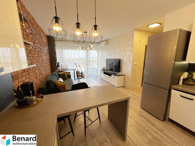 KOŠICE-2 IZBOVÝ BYT,NOVOSTAVBA,KOMPLET ZARIADENÝ,VL.PARK. MIESTO - Obývacia izba s barovým pultom, podlahou s dreveným dekorom a tehlovým akcentom.