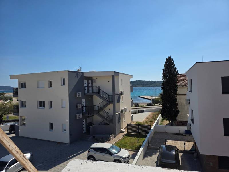 CHORVÁTSKO - Apartmány 40 m od mora vo výstavbe - SRIMA, VODICE - Budovy blízko mora v meste Srima, s výhľadom na pobrežie a automobilmi na parkovisku.