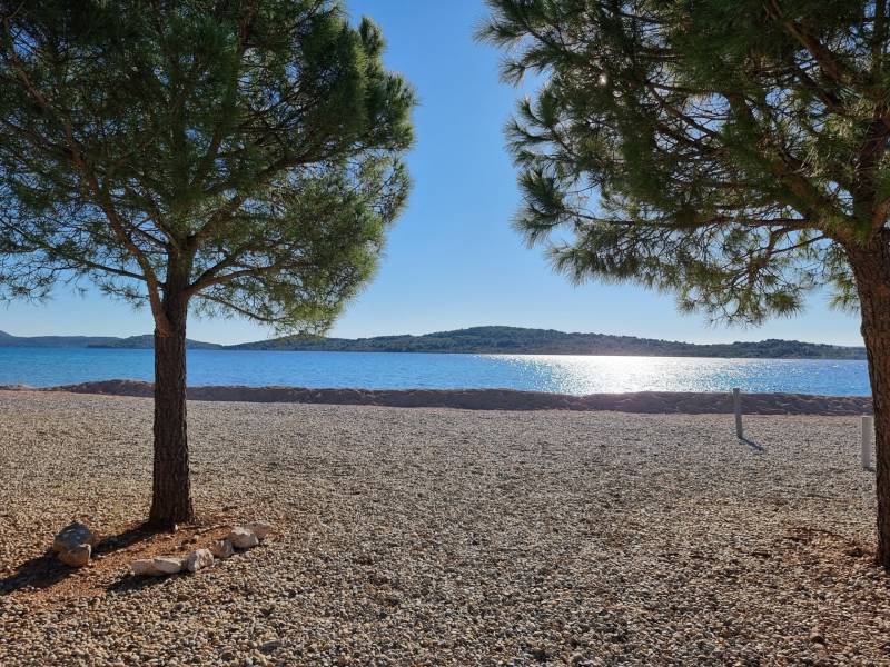 CHORVÁTSKO - Apartmány 40 m od mora vo výstavbe - SRIMA, VODICE - Pokojný výhľad na kamenistú pláž s azúrovým morom, obklopený stromami.
