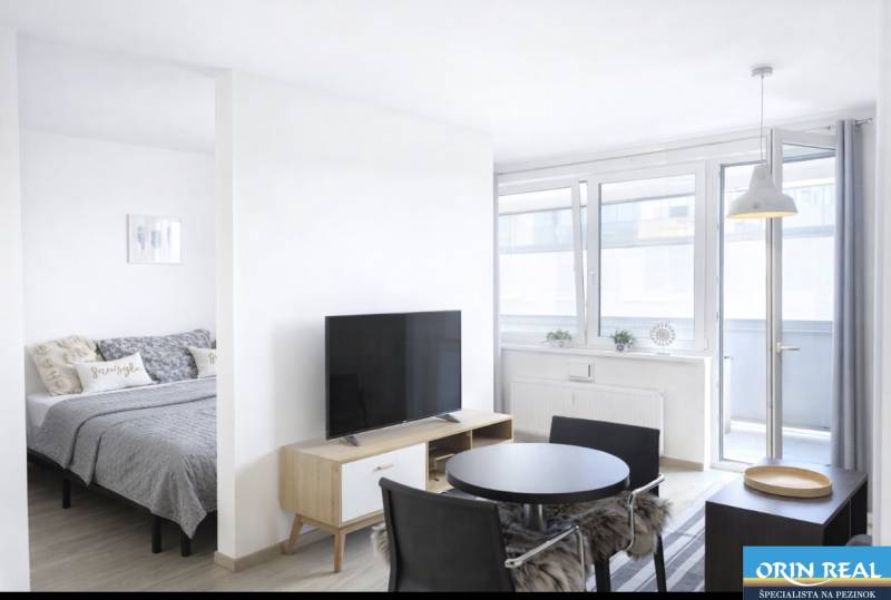 Na predaj 1,5 izbový apartmán v BA III Malokrasňanská 42,34m2 - Svetlá obývacia izba v 2-izbovom byte s televízorom a jedálenským stolom.