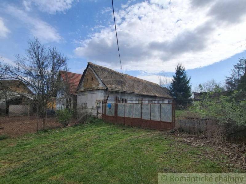 Vymeňte mestský hluk za ticho Bystričky: Domček s dušou a potenciálom - Rodinný dom v Ozdíne, obklopený záhradou a stromami, pod modrou oblohou.