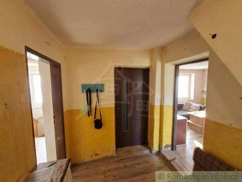 Vymeňte mestský hluk za ticho Bystričky: Domček s dušou a potenciálom - Interiér rodinného domu s podlahou s dreveným dekorom, žlté steny, vešiak, pohovka.